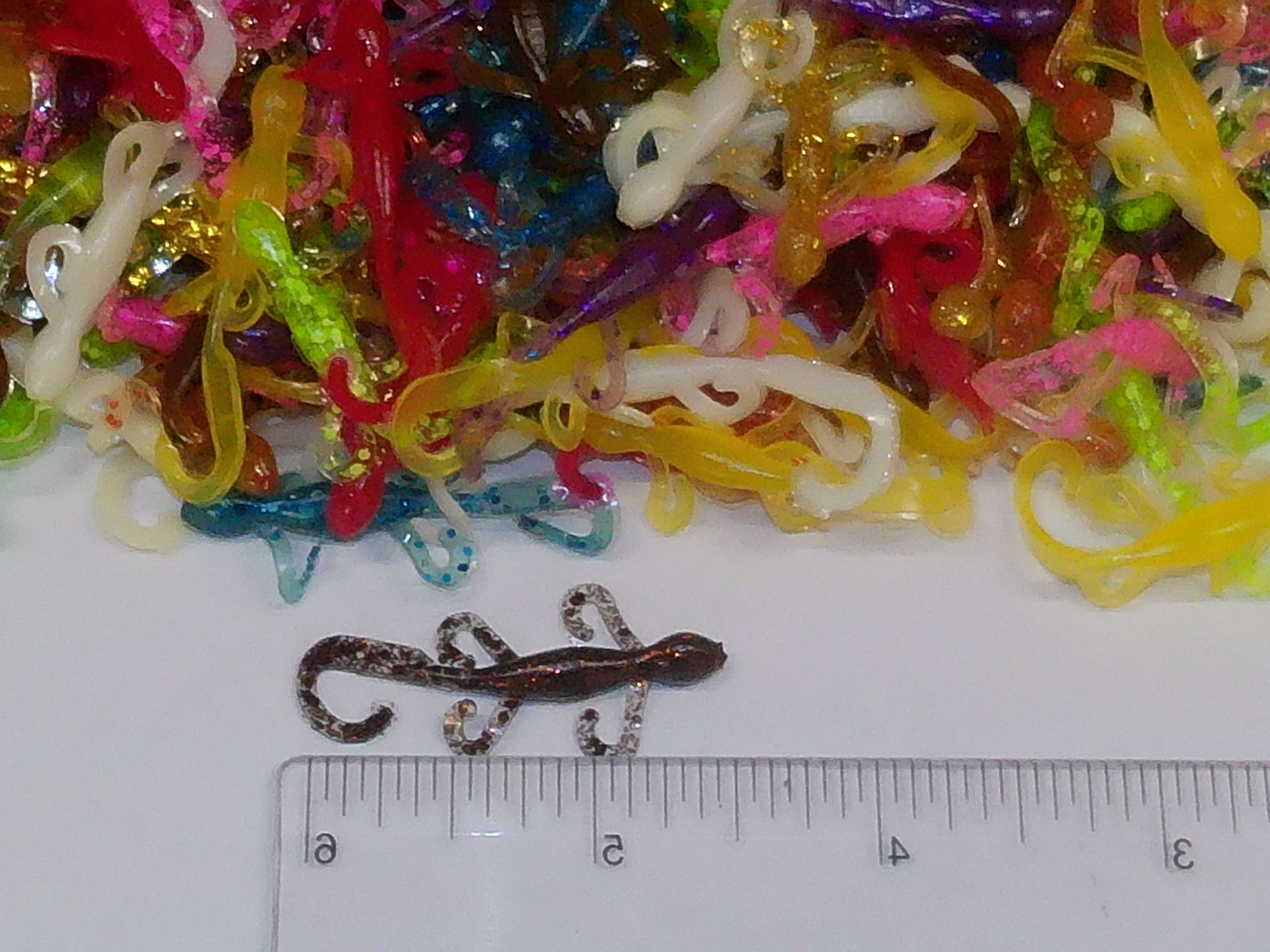 Assorted 2.5 inch micro torpedo soft plastic lures, one on ruler