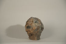 Abstract plaster head sculpture with a rough, crumbling texture in earthy beige and grey tones, evoking erosion and decay.