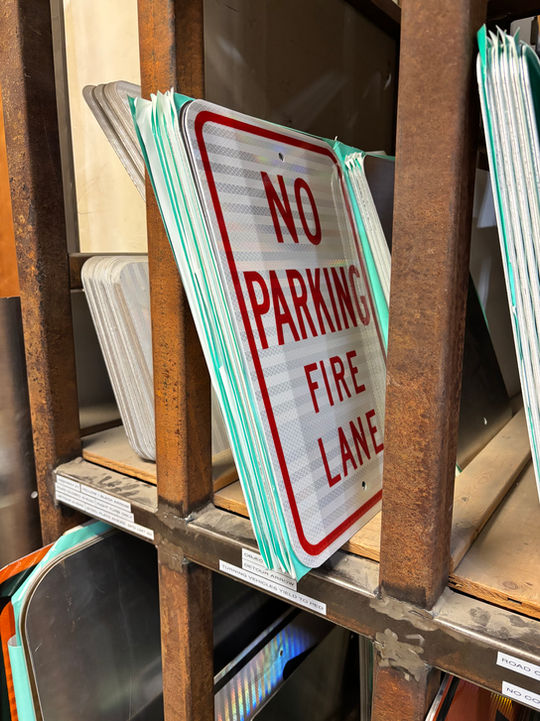 Stack of 'NO PARKING FIRE LANE' signs on a shelf