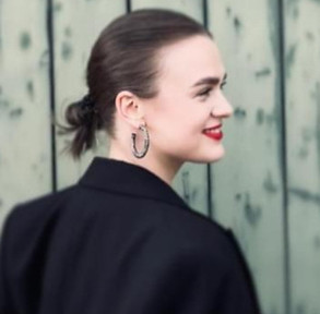 Young mezzosoprano ANNA STEPANETS - Ensemble Landestheater Flensburg - young lady, in the profile, hair bunded in the neck, dark led lipstick, big creoline, black jacket over the shoulder
