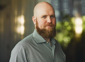 Portrait - Countertenor ERIC JURENAS - bold head, long full beart, checked white-green shirt, looking into the camera.
