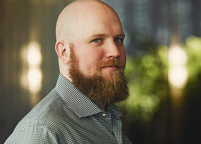 Portrait - Countertenor ERIC JURENAS - bold head, long full beart, checked white-green shirt, looking into the camera.