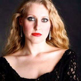 Soprano ARMINIA FRIEBE in a black dress, nearly shoulder-free, with open gold-blond hair long earings, red lips and beautiful big eyes.