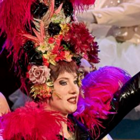Polish Mezzosoprano ANNA GRYCAN as Prince Orlofsky in J. Strauß's "The Bat". Black glitter shirt, pink/red fether boa, red-hair-wig and a huge hat with many feathers and many flowers in red, pink, beige, rosé, yellow and green
