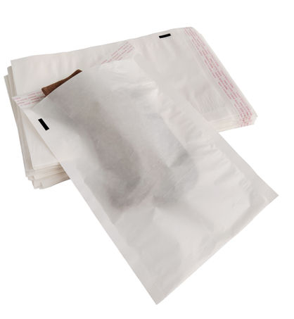 Two translucent glassine auto-bagging bags on a white table, one slightly angled, each holding apparel with the red self-seal flap visible at the top.