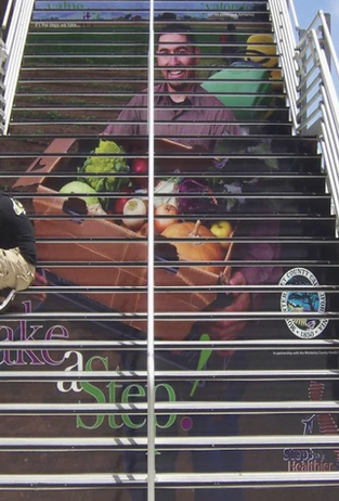 Mural on an outdoor staircase, showing a man holding a box of healthy groceries with the words "Take a Step"