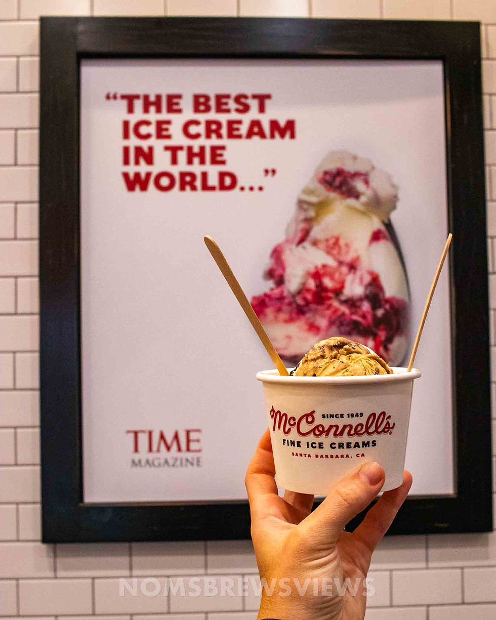 Hand holds McConnell's ice cream in front of a sign reading "The Best Ice Cream in the World..." by TIME. Creamy textures and bright colors.