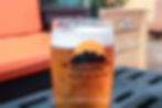 A glass of amber beer with a white foam top, labeled Blackrocks Brewery, Marquette, MI. It's on a patio table with orange seats.
