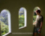 Man in casual attire gazes out arched window at lush green forest. Soft light filters through, creating a serene, contemplative mood.
