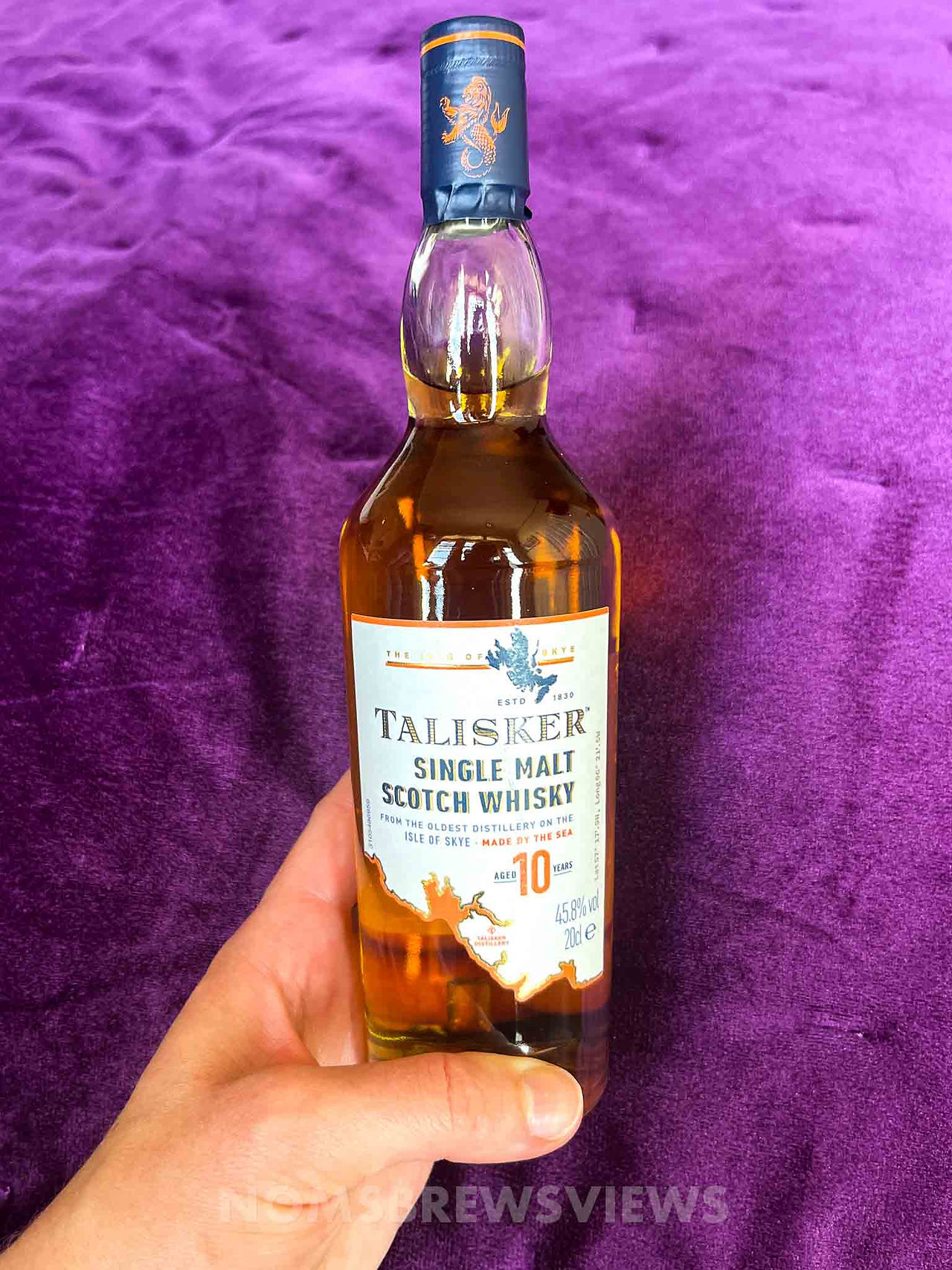 Talisker Single Malt Whisky bottle being held up by a hand with a purple background