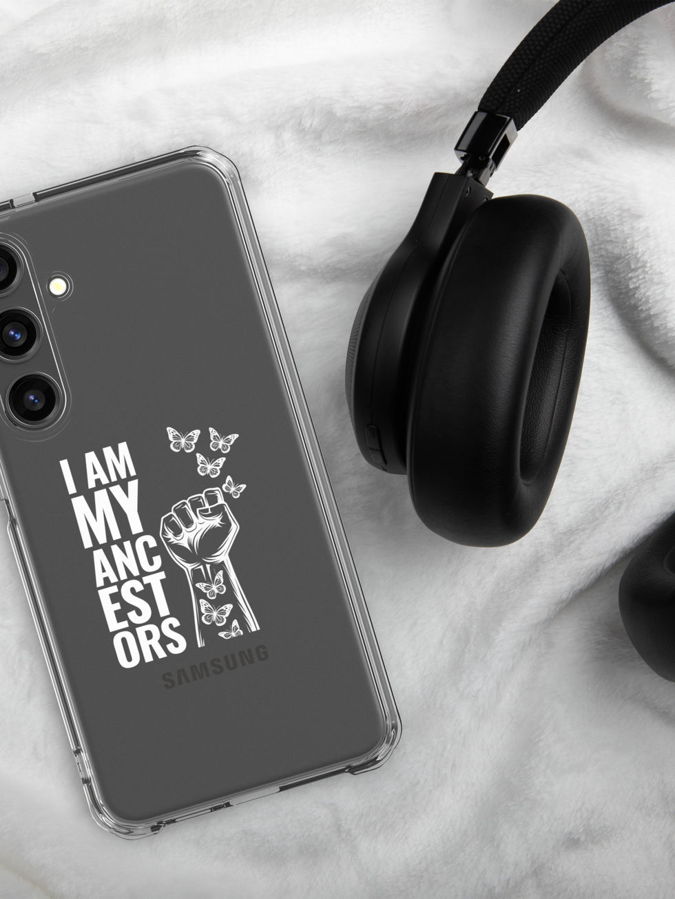 Phone case with text: I am my ancestors, and headphones on a white sheet.