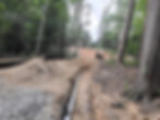 Pipe in an excavated trench beside stone bedding and site access.