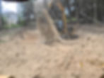 Yellow tracked excavator dumping soil into an excavated area surrounded by trees.