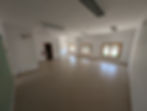 Sala ampla e vazia em imóvel, com paredes brancas e janelas.