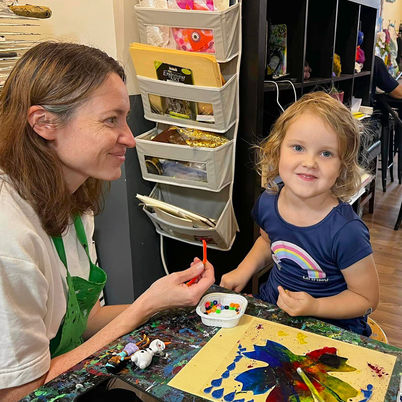 Young girl smiles as she works on art project next to mother.