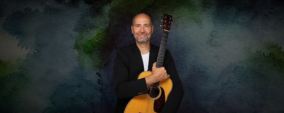 Eddi Hüneke mit Akustikgitarre vor künstlerischem dunkelblauem Hintergrund – Porträt des deutschen Musikers und Sängers in schwarzem Sakko.