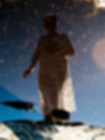 A womans mirror image in a lake, floating flower petal covering the surfaace.