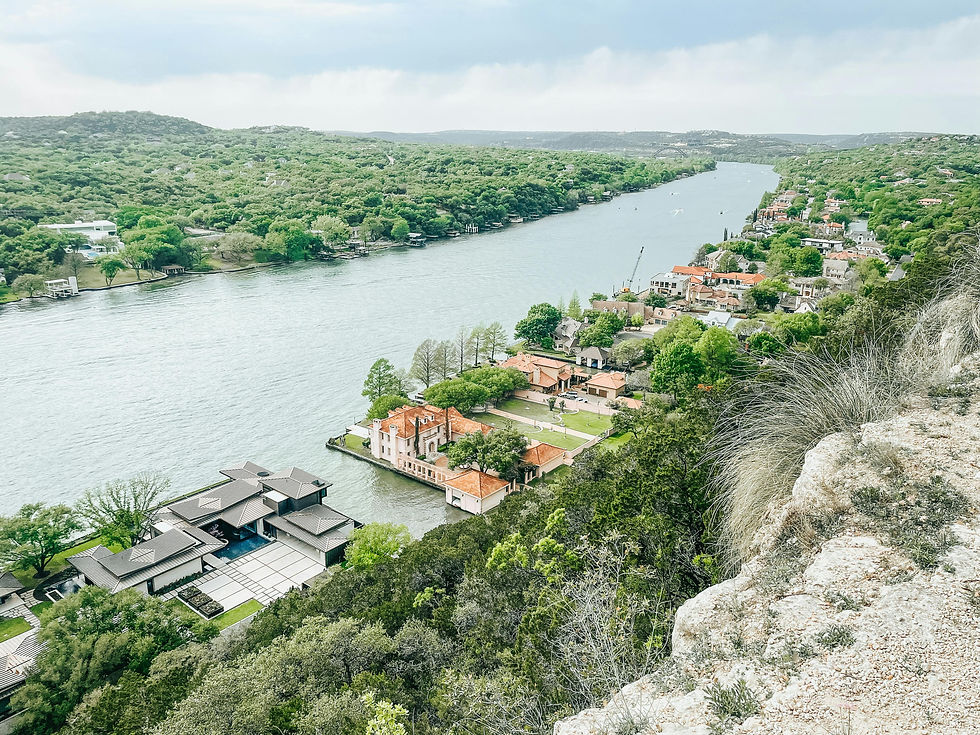 Aerial view of a river with lush green hills and houses with red roofs. Stone cliff in the foreground. Calm and serene atmosphere.