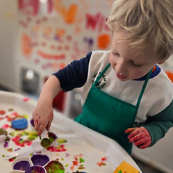 A toddler is havin fun with paint and toys.