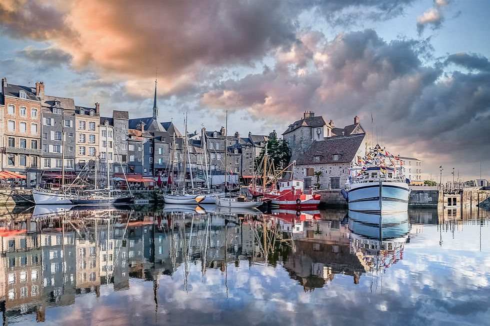 Honfleur harbour at dusk, Normandy, with colourful fishing boats and waterfront buildings reflected in calm water.