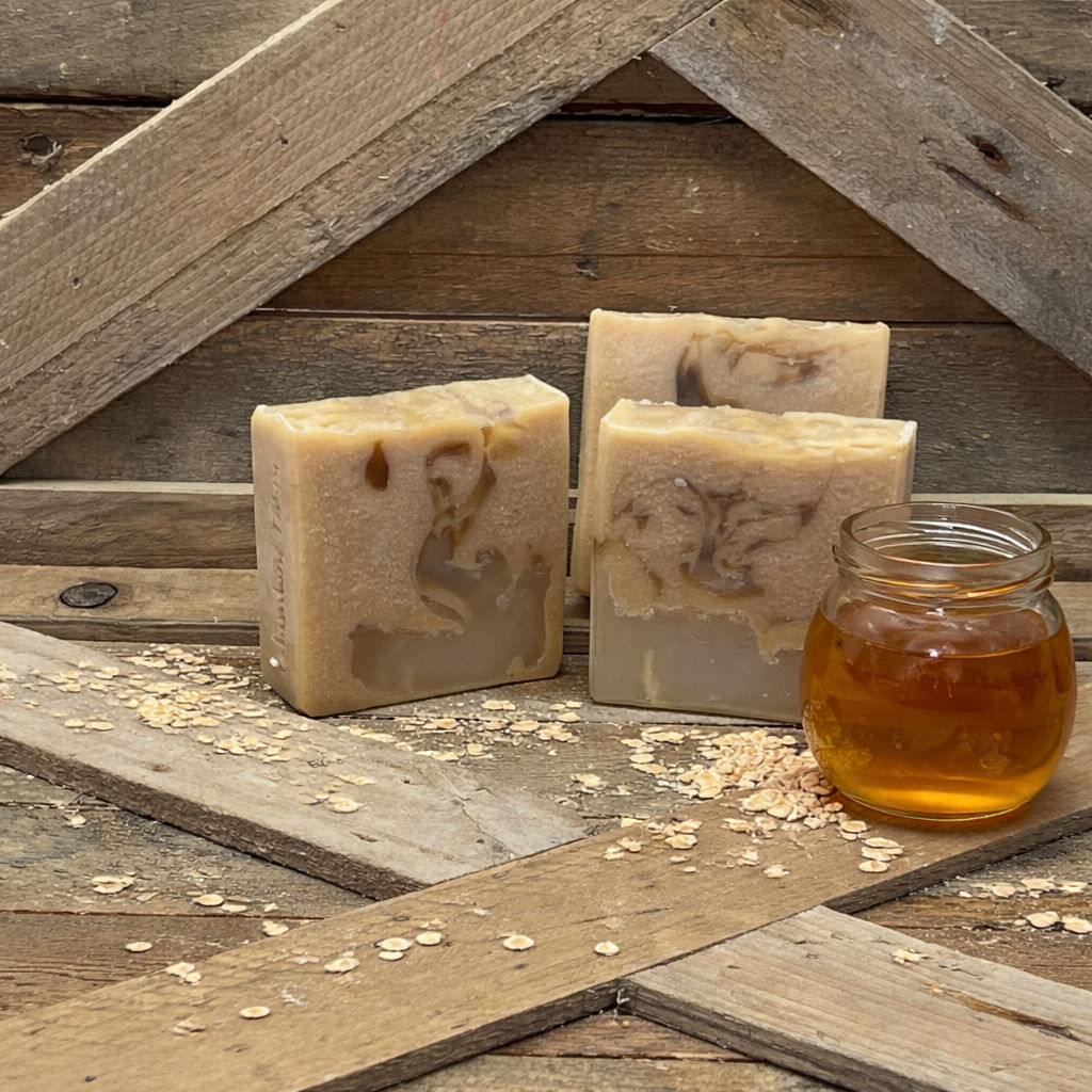 Three bars of light caramel colored soap mixed with clear glycerine soap. A jar of honey next to them along with a few oats