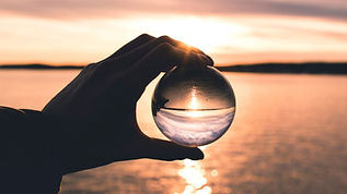 a hand holding a sphere reflecting the image of a calm lake