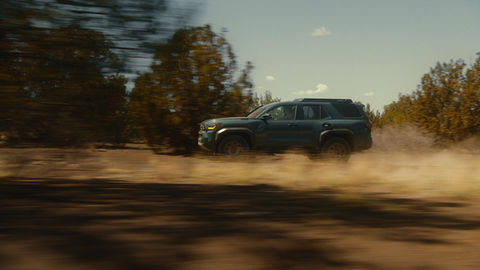 SUV driving through desert trees with dust trail