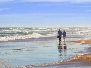 A couple walks hand in hand along the shoreline on a sunny day.