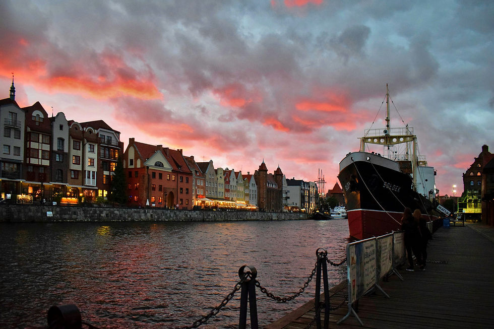 Evening view of the Motława River in Gdańsk as the sun sets behind the historic waterfront.