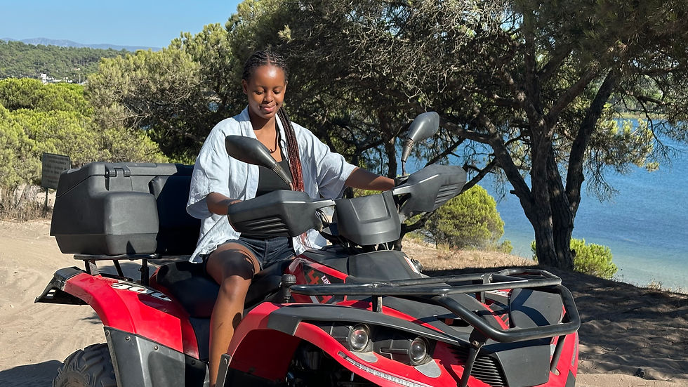 Woman rides a red ATV on a sunny coastal dirt road, with pine trees and blue sea in the background.