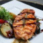 Grilled Carp with sauce on a white plate, accompanied by roasted potatoes and fresh salad.