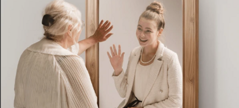 Young woman looking at her elderly reflection in a mirror, symbolizing the long-term security and protection offered by whole