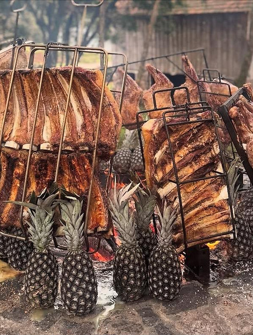 Costelão preparado no fogo de chão, acompanhado de abacaxis assados, na experiência gastronômica Gaita e Assado.