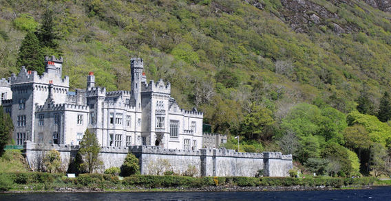 Vue d'ensemble de l'abbaye de Kylemore en pierre grise au pied d'une immense montagne verdoyante et rocheuse en Irlande.