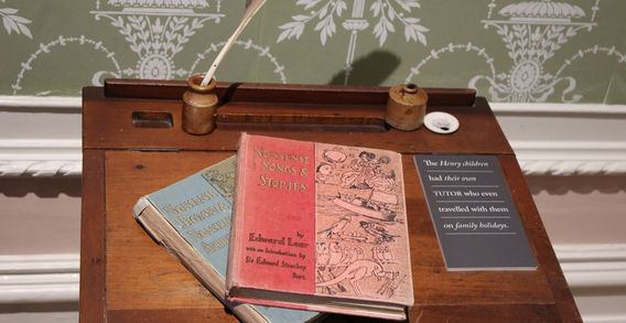 Deux anciens livres de contes d'Edward Lear posés sur un pupitre d'écolier en bois avec un encrier devant un papier peint vert à l'abbaye de Kylemore.