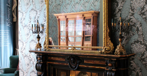 Un grand miroir doré sculpté suspendu au-dessus d'une cheminée noire dans une pièce au papier peint damassé vert à l'abbaye de Kylemore.