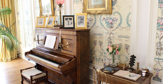 Un piano droit ancien en bois avec sa banquette dans un salon d'époque au papier peint fleuri à l'abbaye de Kylemore.