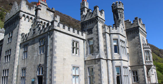Vue en contre-plongée de la façade en pierre grise de l'abbaye de Kylemore avec ses fenêtres et ses tours crénelées sous un ciel bleu en Irlande.
