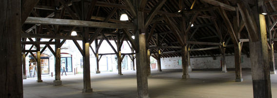 Vue intérieure des Halles médiévales de Clisson, mettant en avant la charpente en bois sombre et les jeux de lumière entre les piliers.