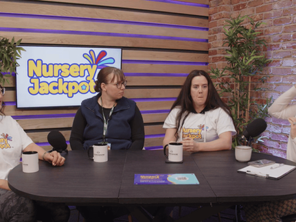 Four women sit at a round table with mugs and microphones, discussing "Nursery Jackpot." The setting has brick walls and plants.