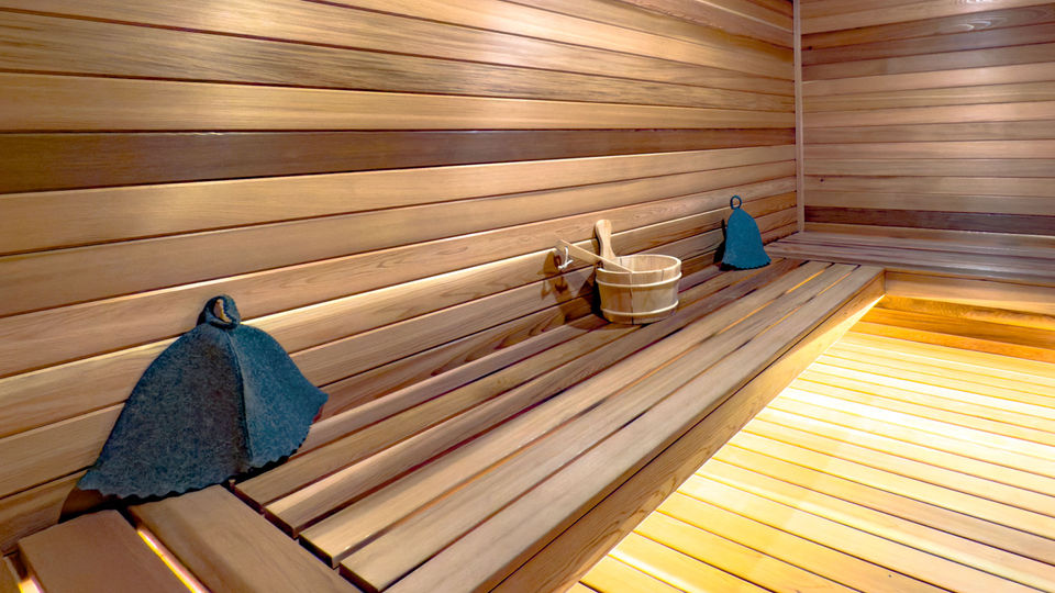interior of sauna with sauna caps and bucket placed on a single tier cedar bench and LED accent lighting