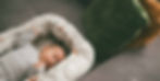 Newborn baby peacefully sleeping in a woven bassinet beside sage green pillows, soft natural light. Soul Work Osteopathy infant care.