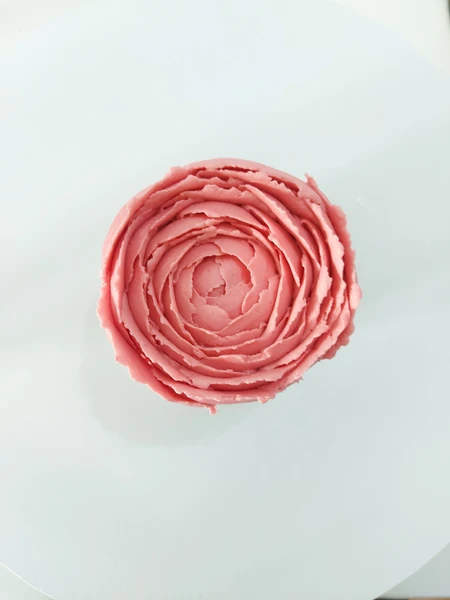 A piped closed peony buttercream flower on a cupcake