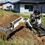 Thumbnail: Man operating Bobcat - E10e Minigraafmachine digging a trench on grassy terrain. De Jong Techniek.