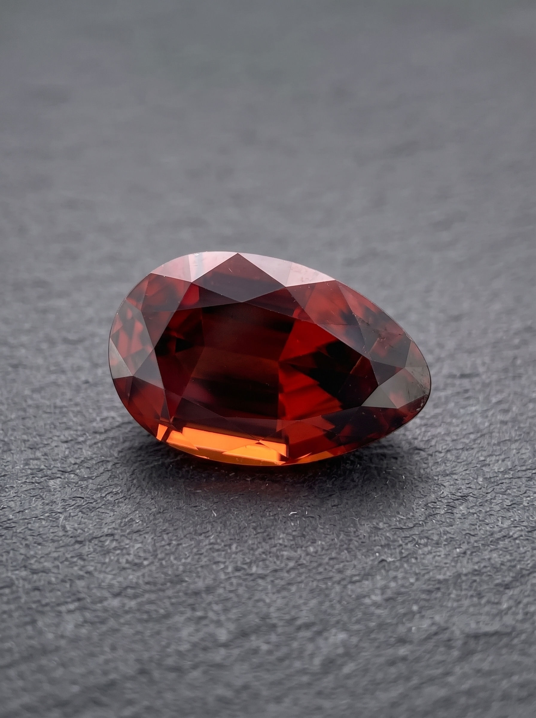 Natural 5.73 ct Mozambique zircon in a pear cut with warm ember-red color and wine tones.