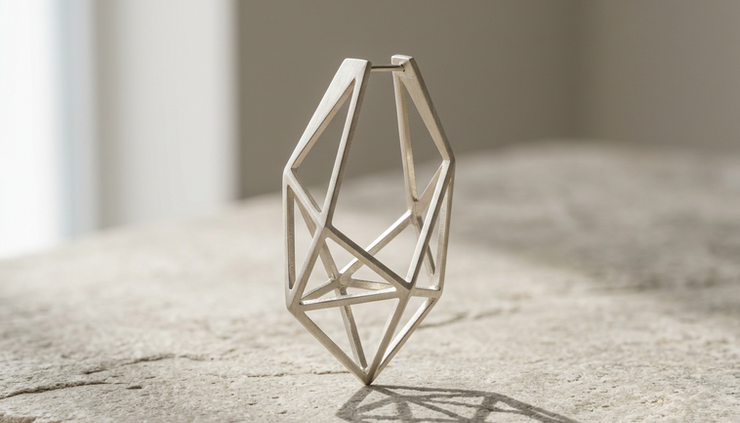 Three-quarter view of a minimal architectural earring standing upright with light passing through its hollow form.