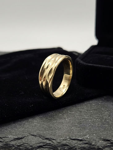 Gold ring with wavy bands on black velvet display, lit against a soft gray background.