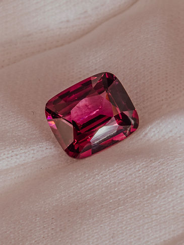 Close-up of a faceted deep pink Umbalite Garnet gemstone resting on a white gloved hand, sparkling against a soft ivory background.