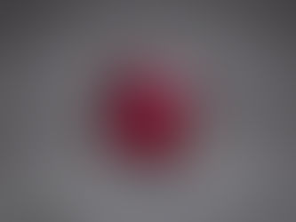Faceted red gemstone on a gray textured surface, sparkling under light with no text visible.