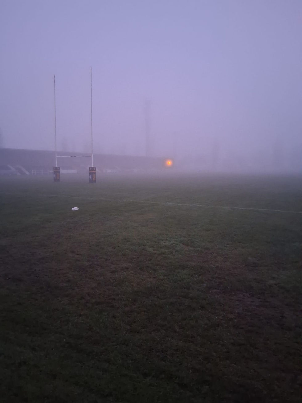 A rugby pitch with a solitary ball, rugby post and light from the far end of the stands